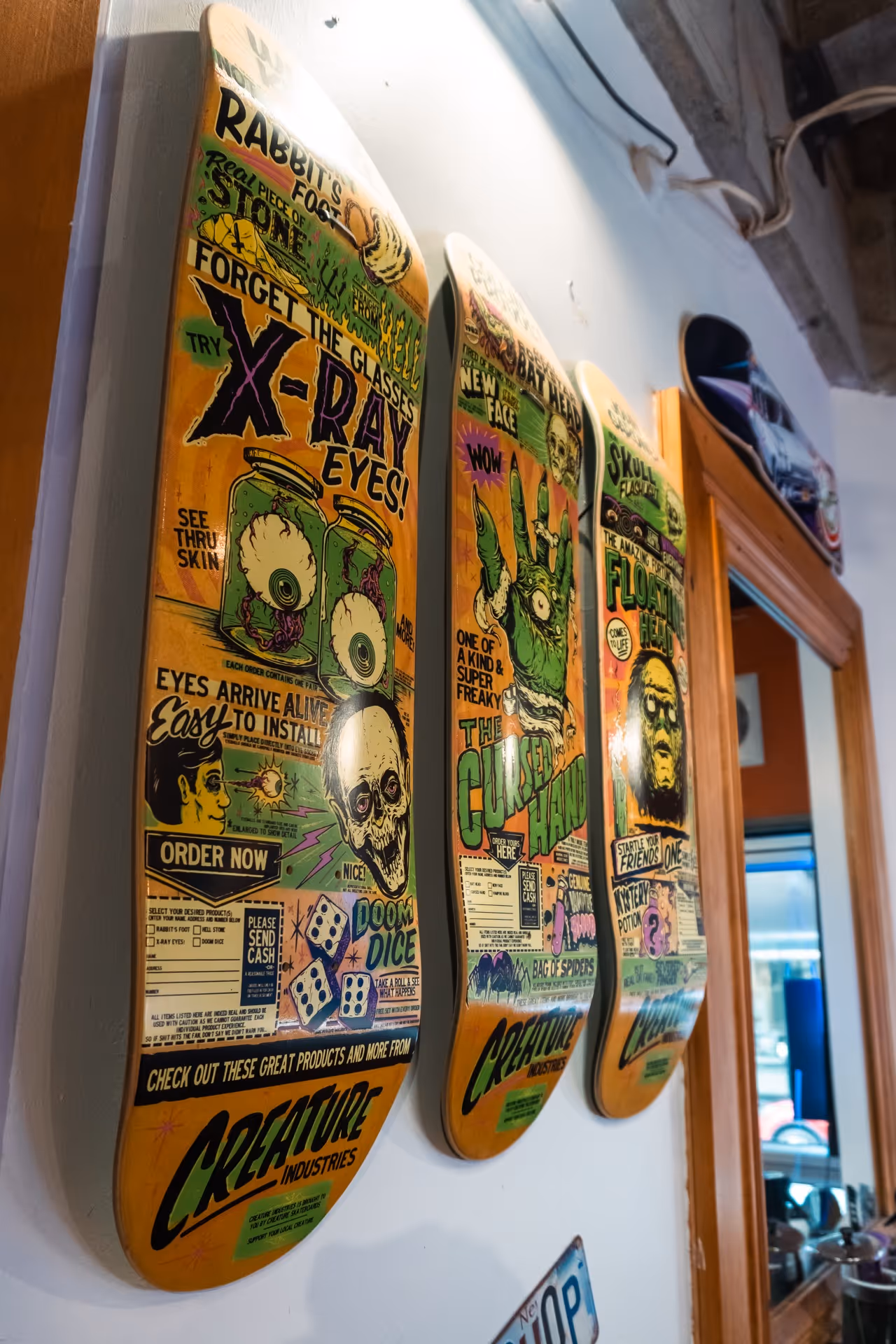 Three colorful skateboard decks with horror-themed vintage comic-style graphics mounted on a white wall.